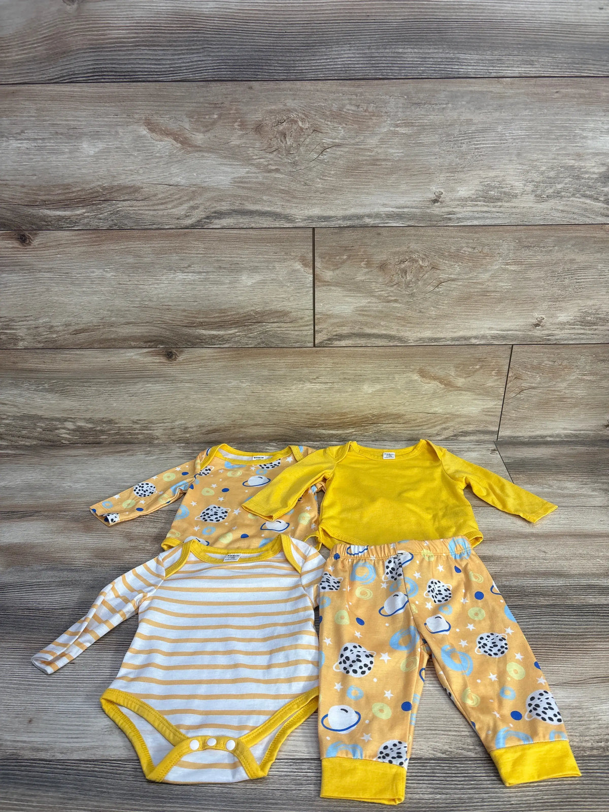 Top view of Shein four piece yellow bodysuit and pant set showcasing three long sleeve bodysuits and patterned pants on wood