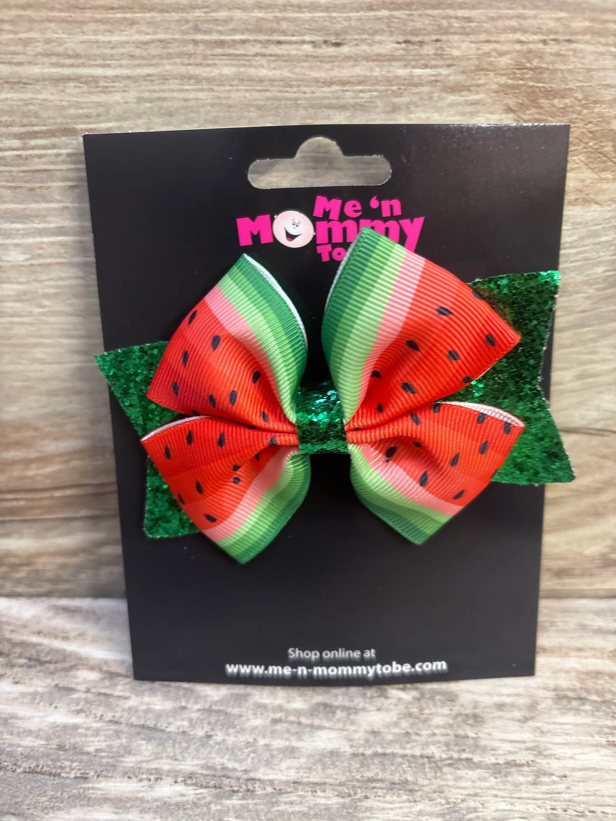 Front view of watermelon hair bow showcasing red-green ribbon with black seed print and green glitter backing on black card