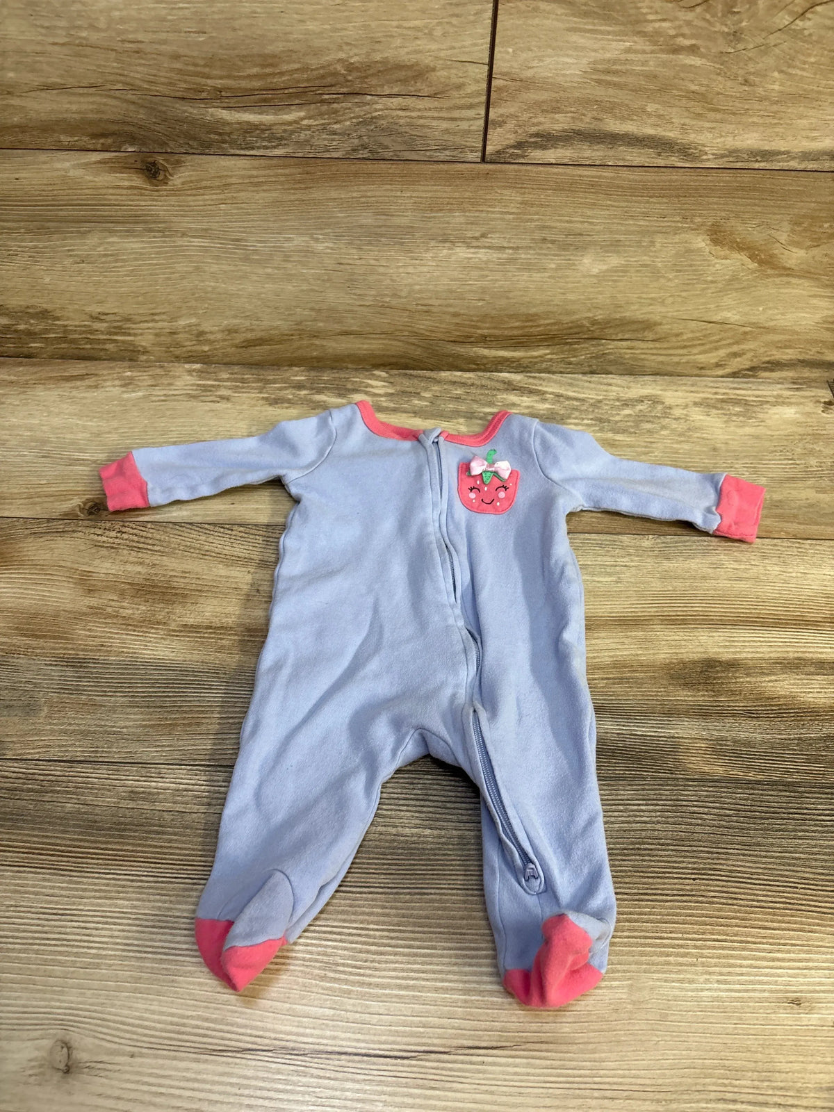 Flat-lay of Koala light blue baby sleeper size 3 months showing front zipper, pink trim and strawberry applique on wood background