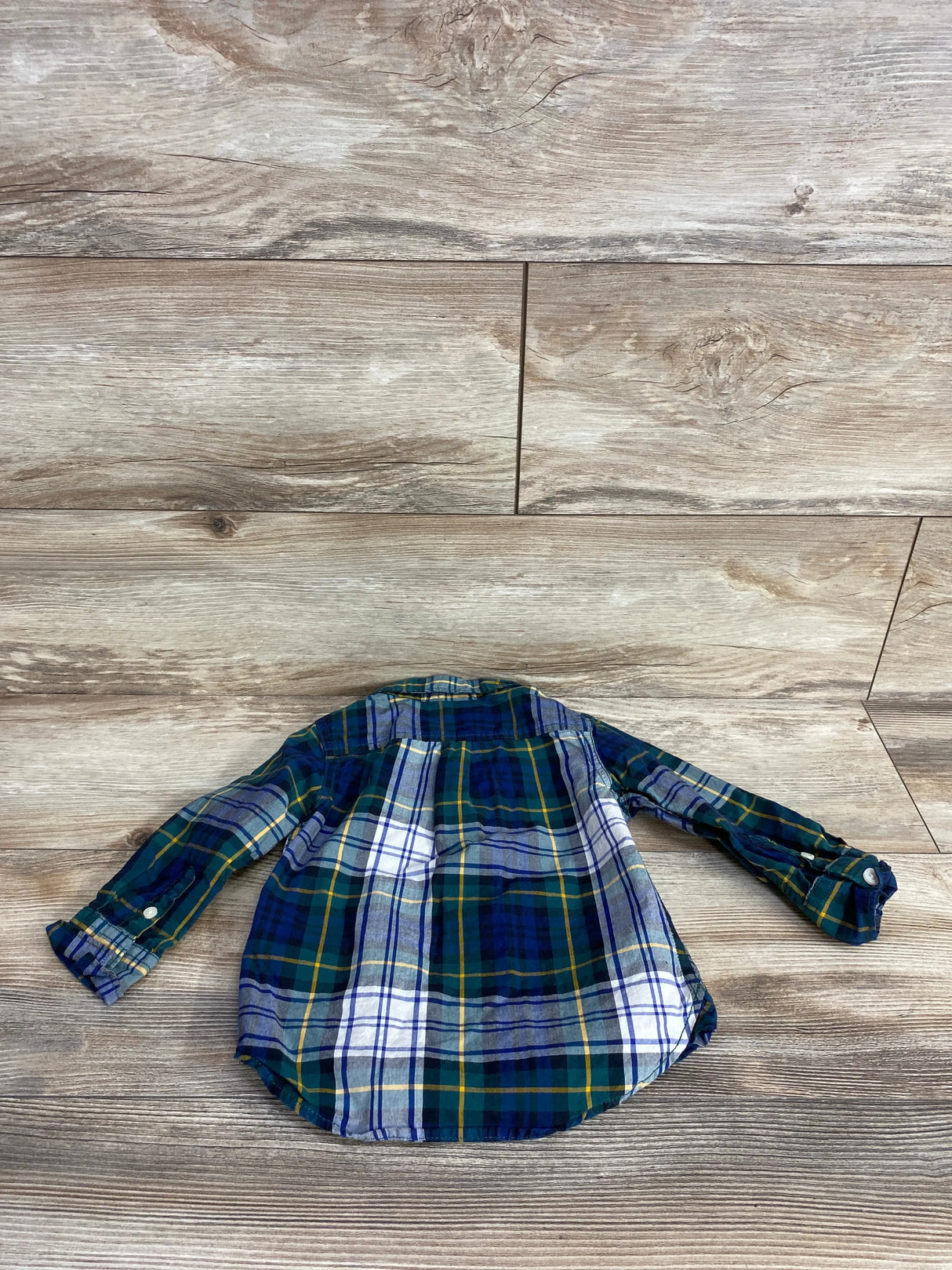 Back view of a green, navy, white, and yellow plaid flannel shirt laid flat on a wooden floor