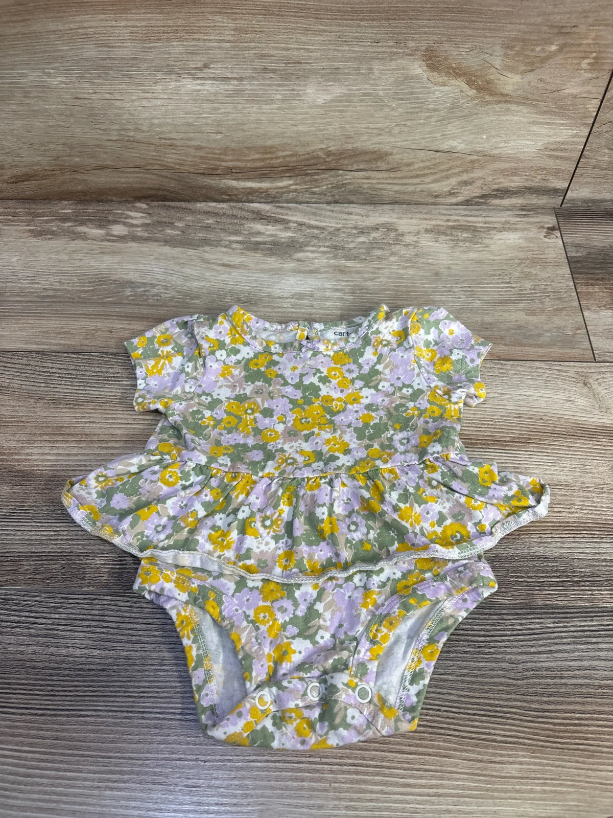 Flat lay of green Carter’s floral bodysuit dress size 3M showcasing ruffled peplum, short sleeves, and three snap crotch closures on wood floor