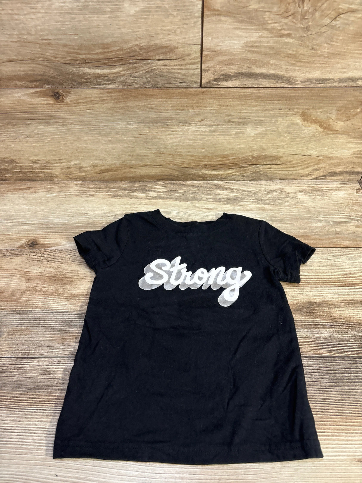 Flat lay of Cat & Jack black short-sleeve toddler shirt (2T) showing white Strong script on the chest on wood background