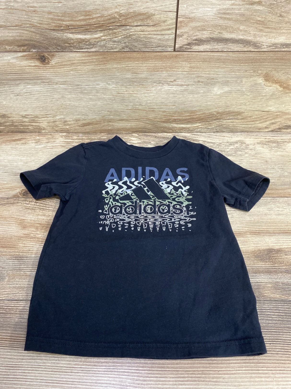 Black Adidas kids graphic t-shirt with logo and sporty design on wood background