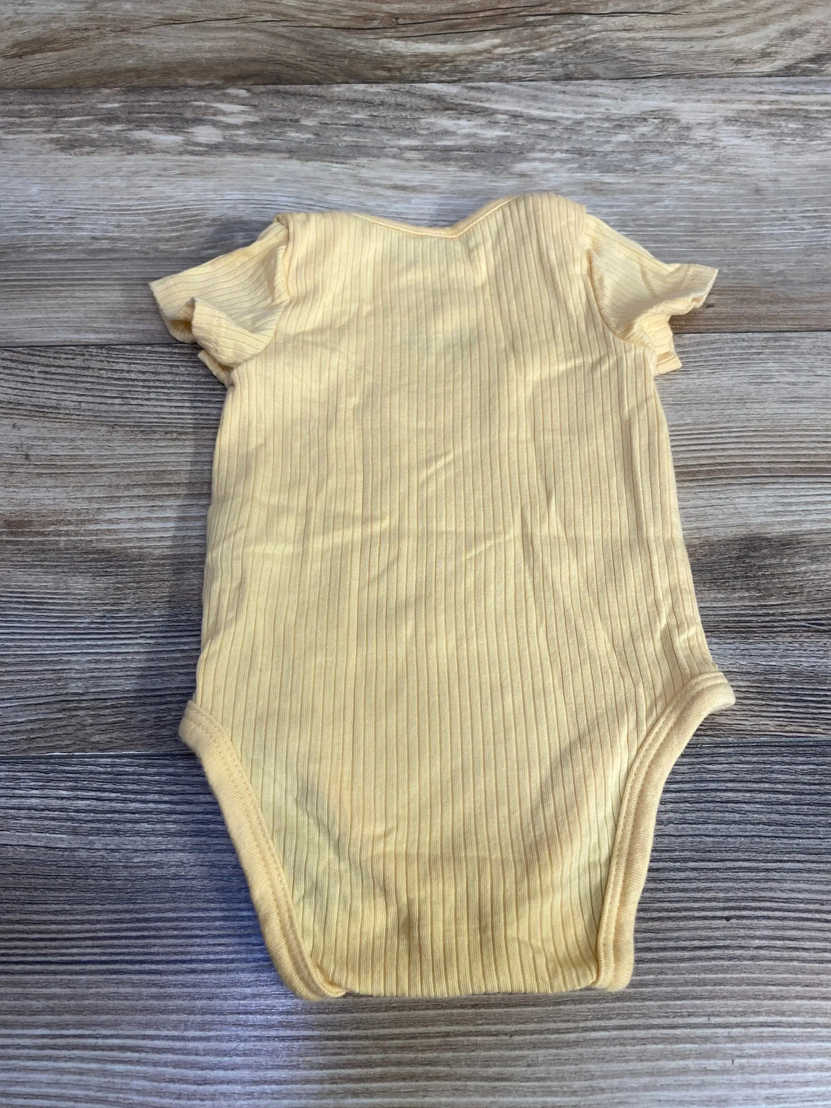 Flat lay of Mori ribbed newborn yellow bodysuit showcasing ribbed texture and short sleeves on wood background