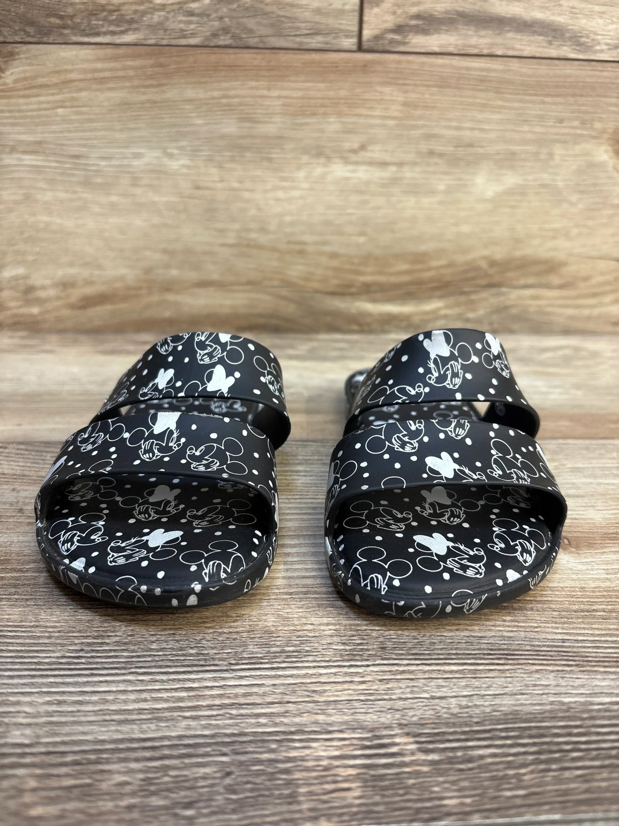 Front view of Mini Melissa Minnie Mouse black slides size 13C showing white Minnie head print and double straps on wood floor