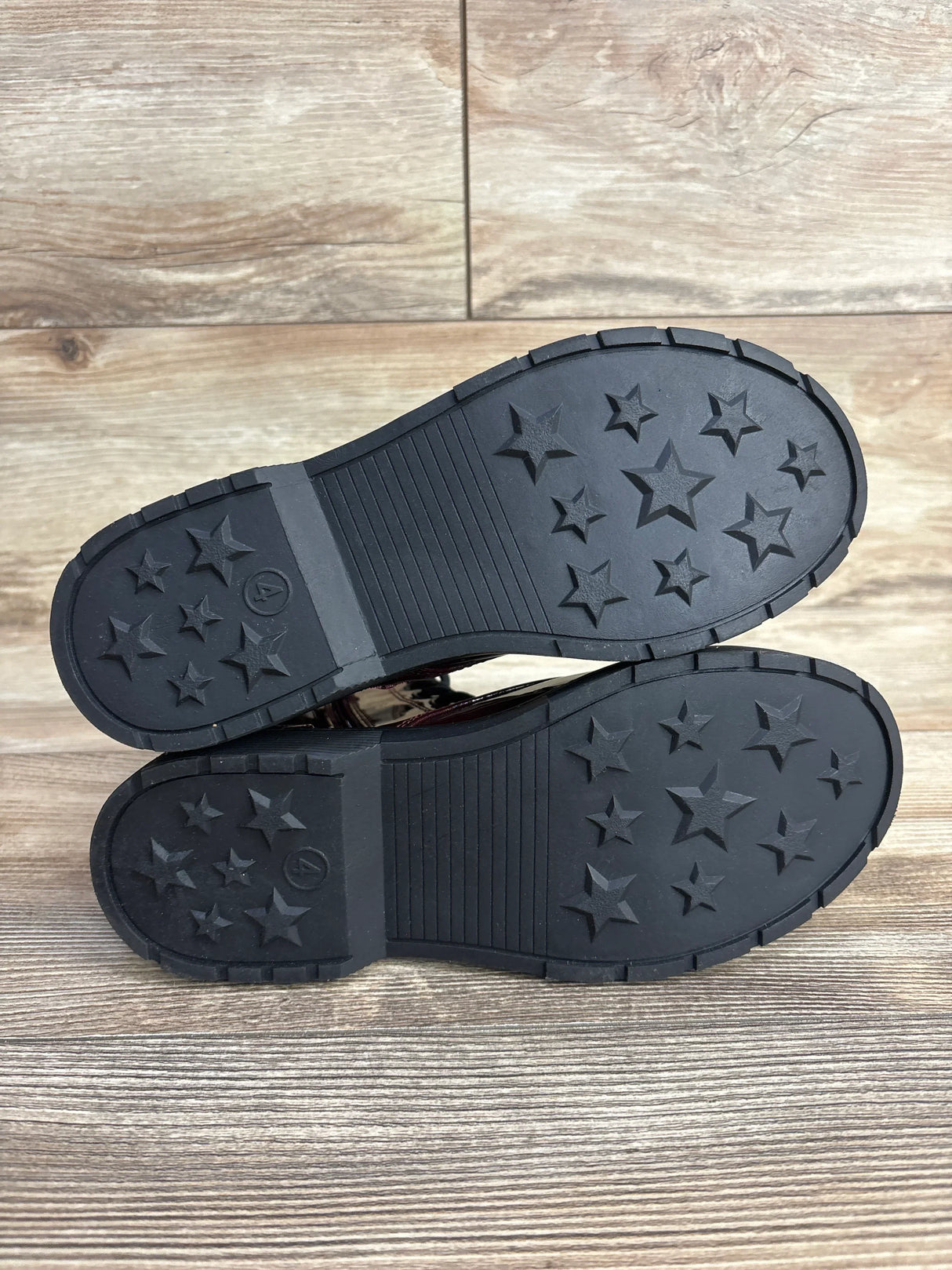 Kids shoes with black rubber soles and star-shaped tread, displayed on wood floor