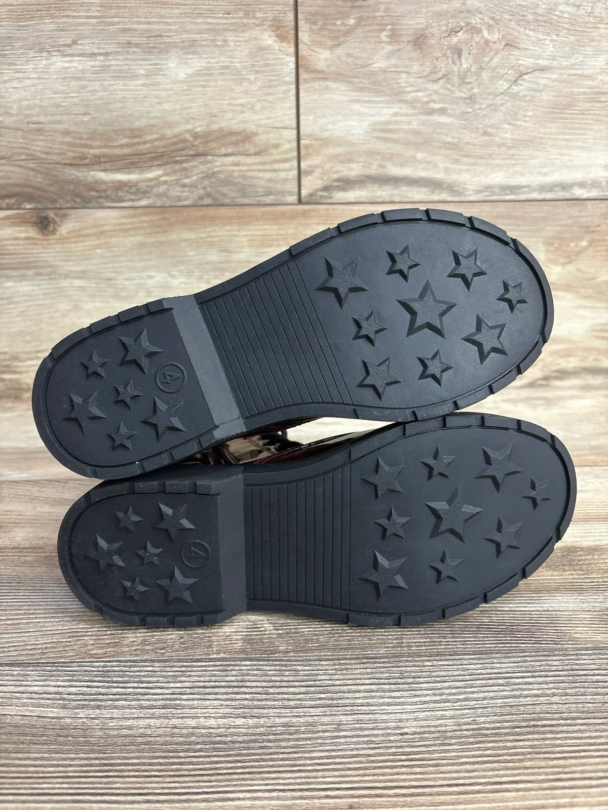Sole view of Art Class Rochelle combat boots (red, size 4Y) showing black rubber soles with star-shaped tread on wood floor