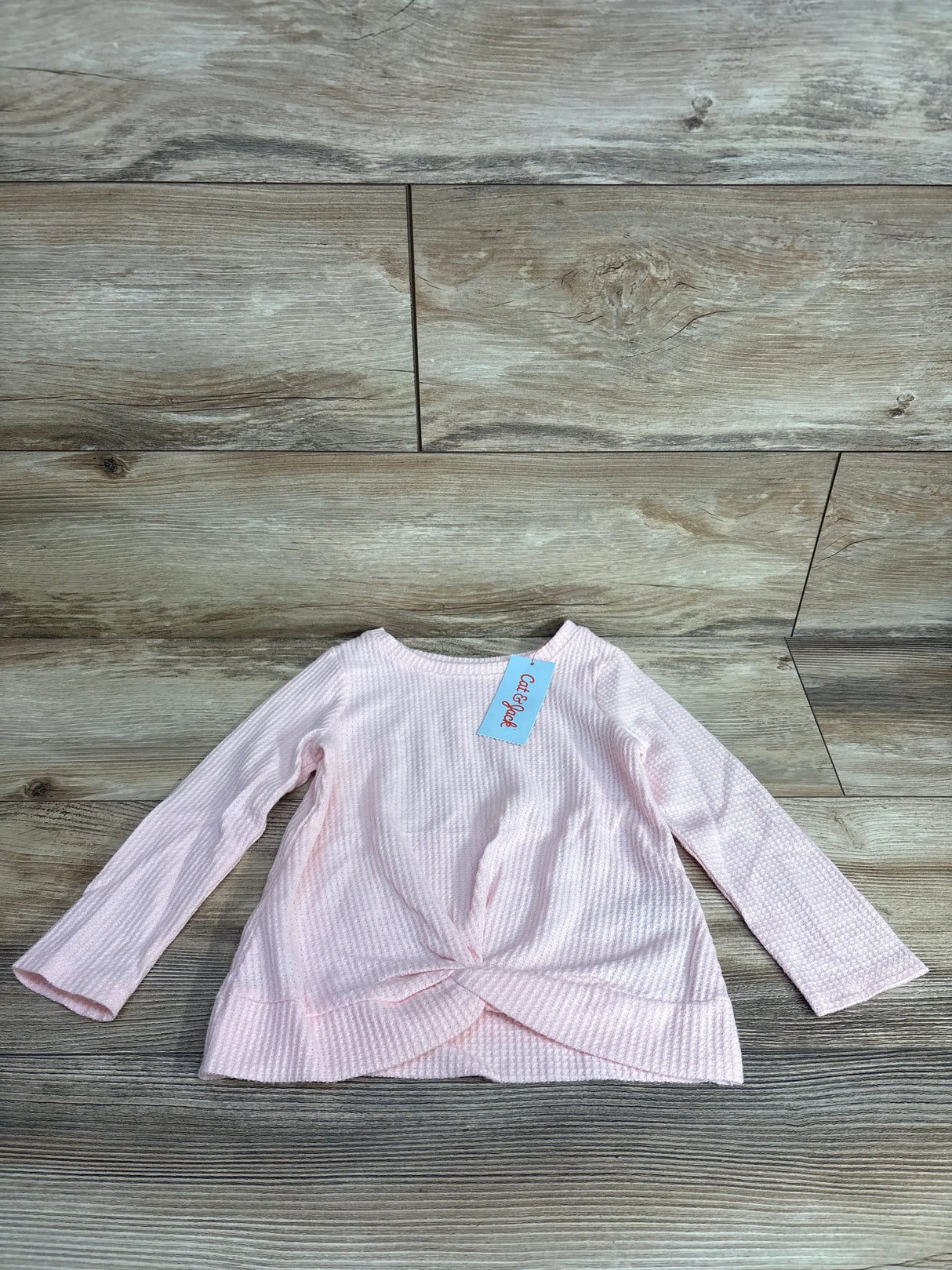 Light pink long sleeve toddler shirt with textured fabric and front twist detail on wood floor