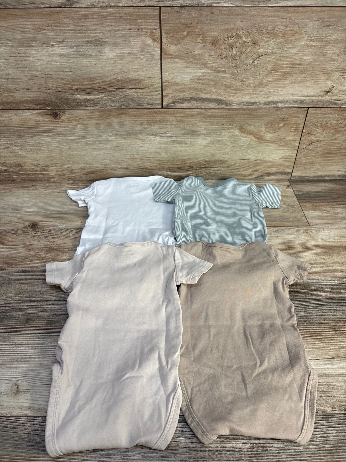 Top-down view of 4 H&M organic kimono bodysuits (beige, light beige, white, green stripe) laid flat on wood background