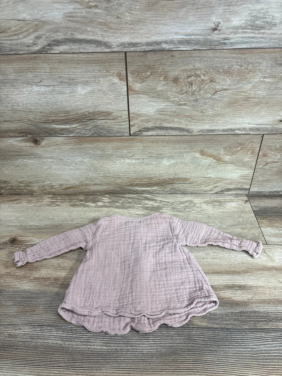 Back view of Jamie Kay Lila muslin blouse in Rose Smoke showing long sleeves and scalloped hem on wood floor