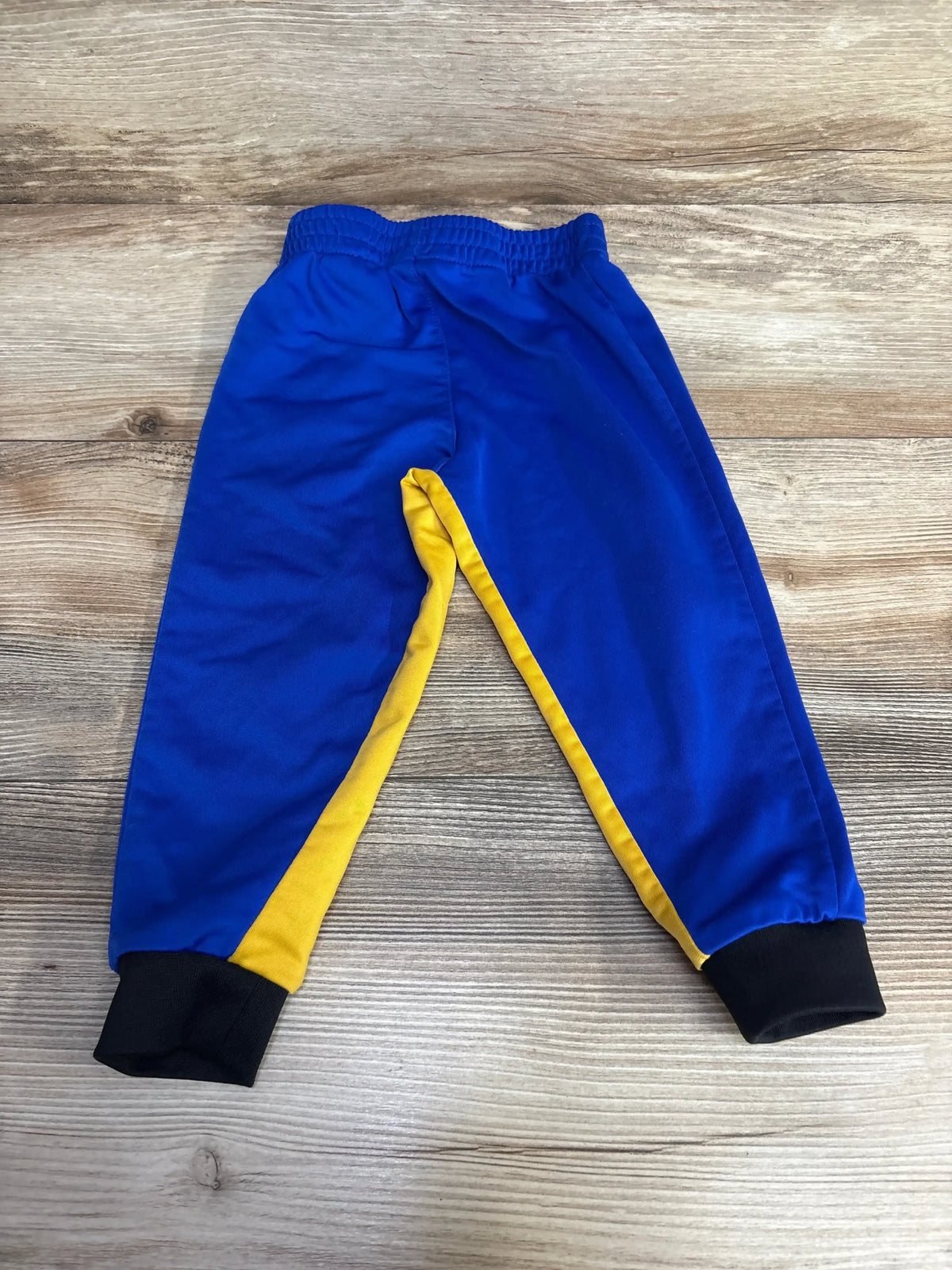 Blue kids sweatpants with yellow side panels and black cuffs on wooden floor