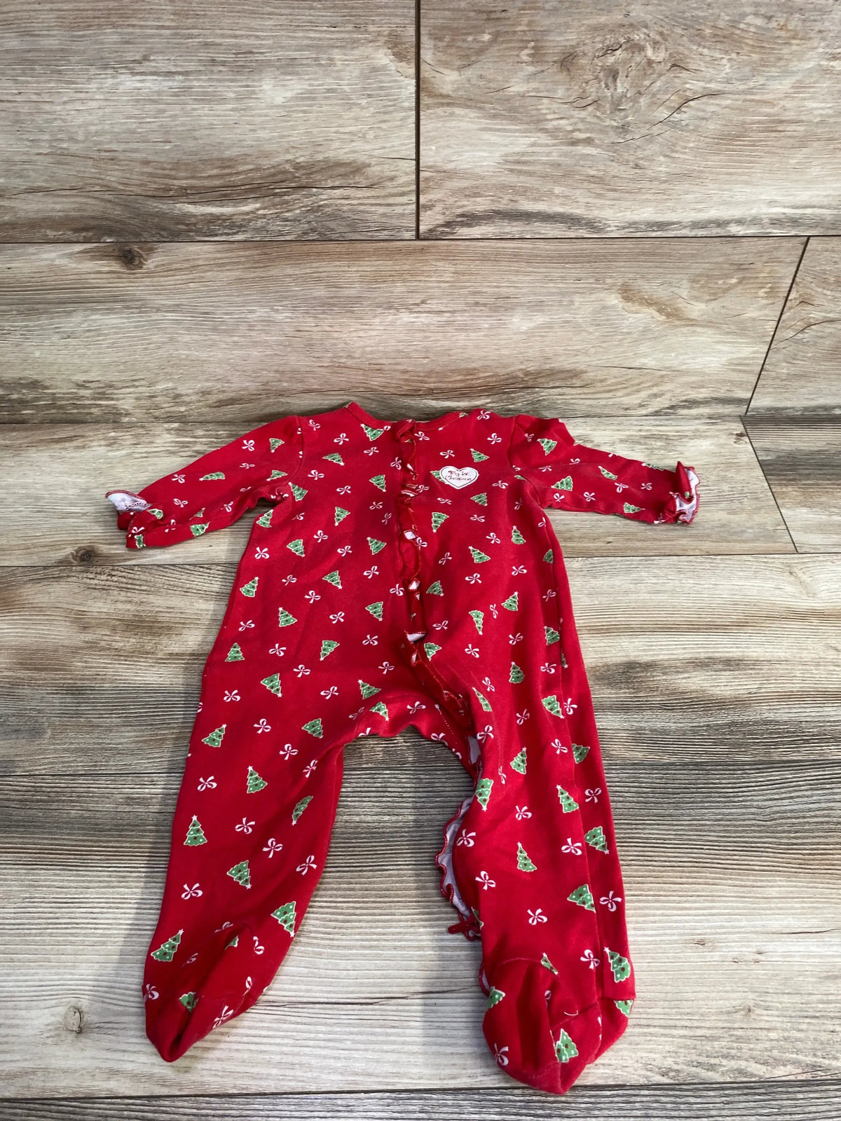 Red baby Christmas onesie with green trees, white bows, and 'My 1st Christmas' heart on wood floor