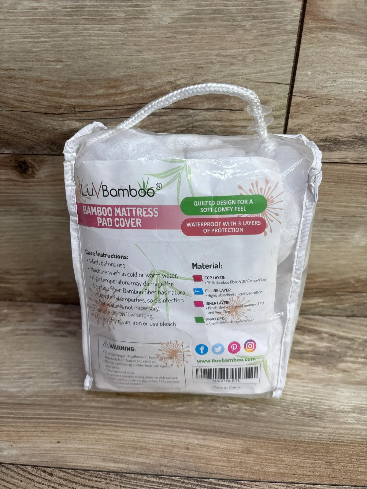 Front view of ILuvBamboo mattress pad cover 2pk in clear packaging showing waterproof 3-layer protection and label on wood
