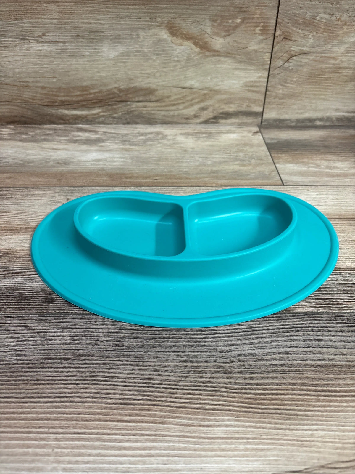 Front view of aqua blue Nuby Sure Grip Silicone Miracle Mat 2-Section Oval Plate showing two sections on wood-grain surface