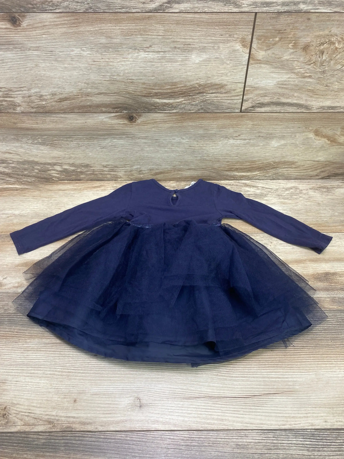 Flat lay of H&M Disney Frozen navy tulle dress showcasing long sleeves, layered skirt, keyhole back on wood background