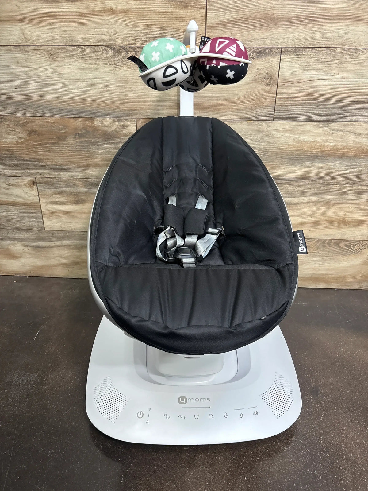 Front view of 4moms mamaRoo multi-motion baby swing with black padded seat, safety harness, and white control base