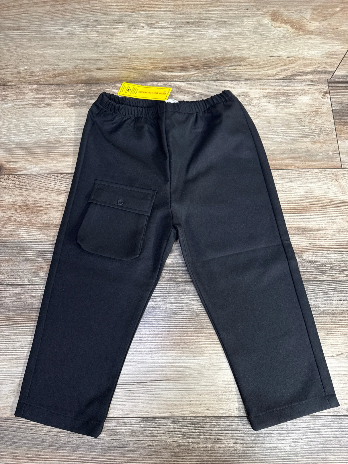 Black children's pants with elastic waistband and flap pocket on wood floor background