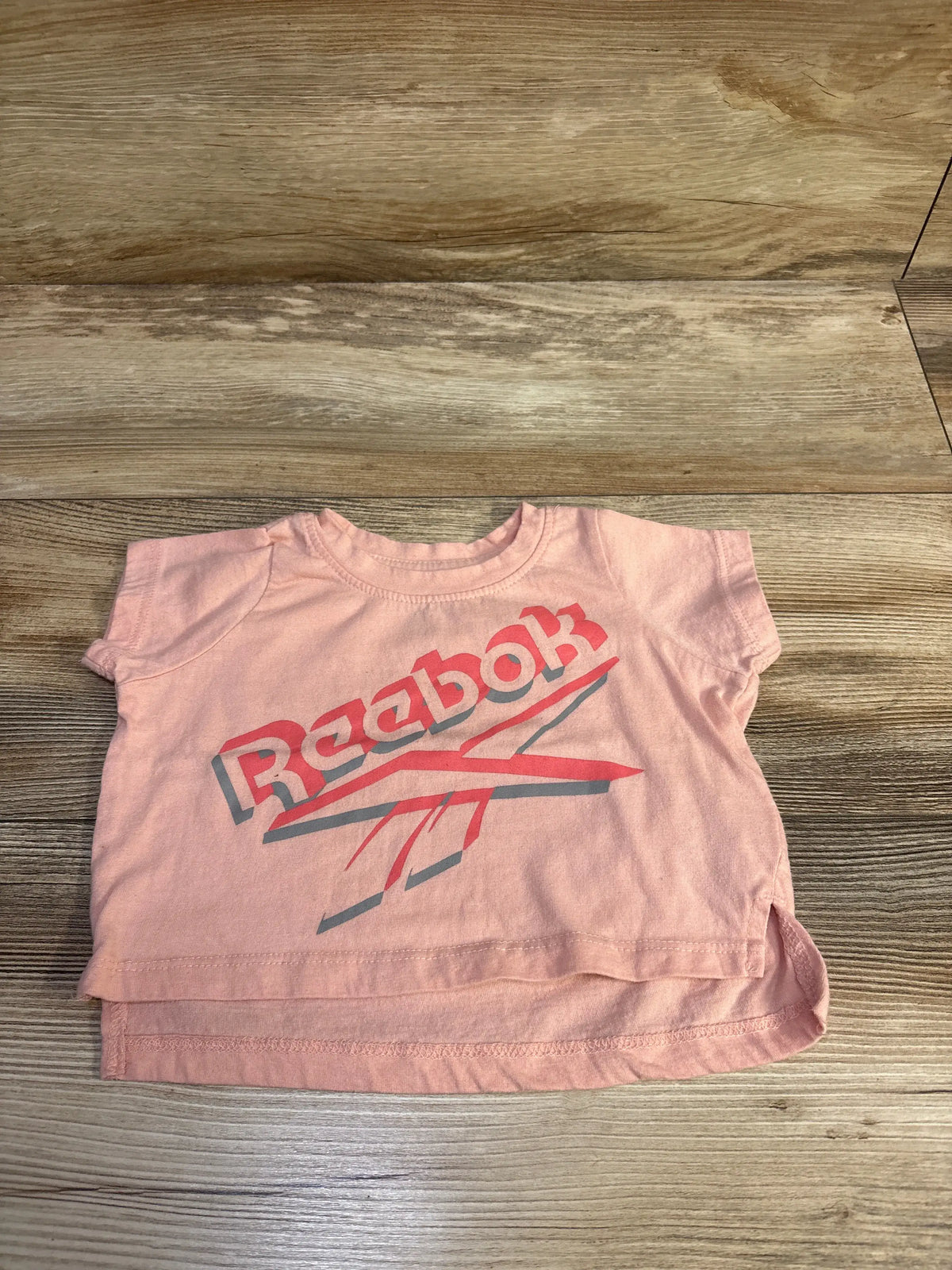 Pink Reebok short sleeve baby shirt size 12m on a wooden surface