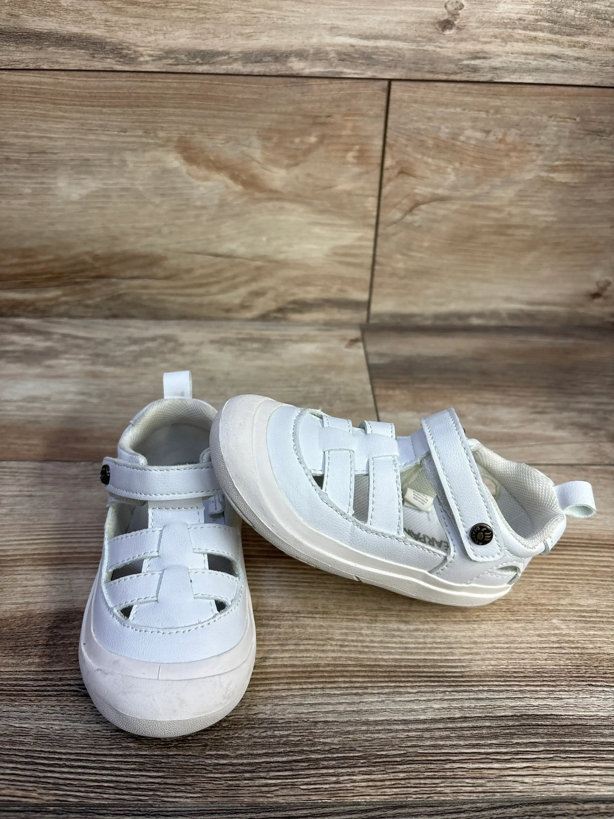 Front and side view of white Bearpaw fisherman sandals showing woven straps, Velcro ankle strap and rubber toe cap on wood background