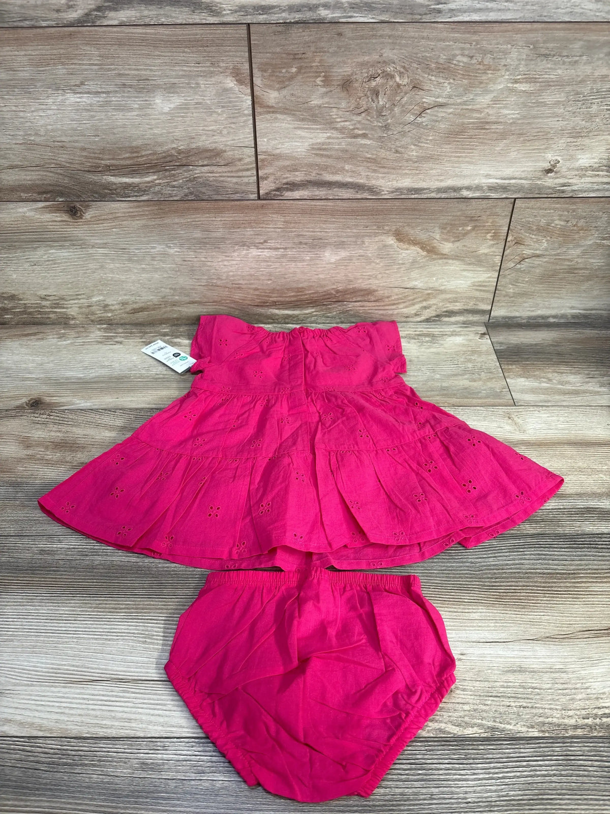 Flat lay of hot pink baby eyelet tiered dress and matching bloomers showing tiered skirt and eyelet details on wood floor