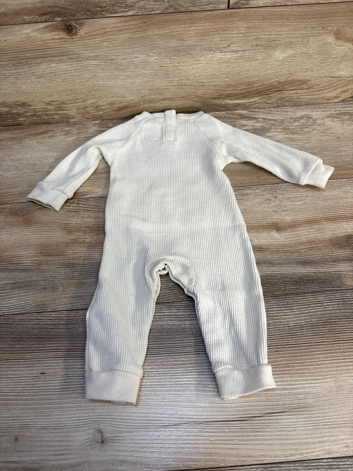 Cream ribbed baby romper laid flat on wooden floor, long sleeve cotton infant clothing