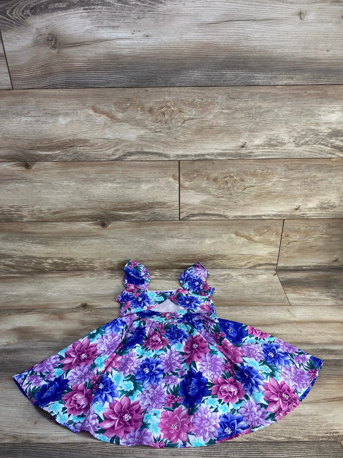 Flat-lay of girls’ blue Janie & Jack floral dress with ruffled cap sleeves and full flared skirt on wood floor