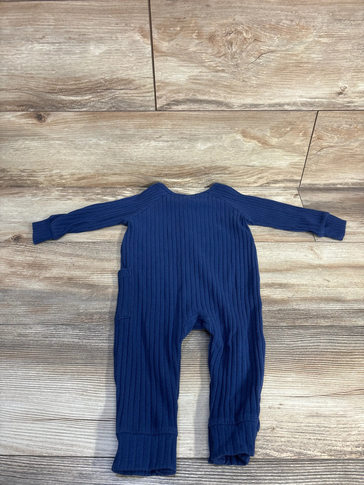 Back flat lay of navy ribbed baby coverall showing long sleeves, cuffed ankles and side pocket on wood floor