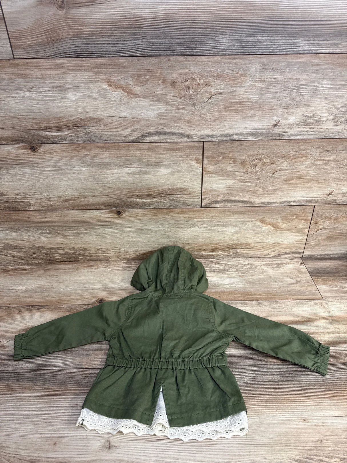 Green hooded toddler jacket with lace trim on wood background