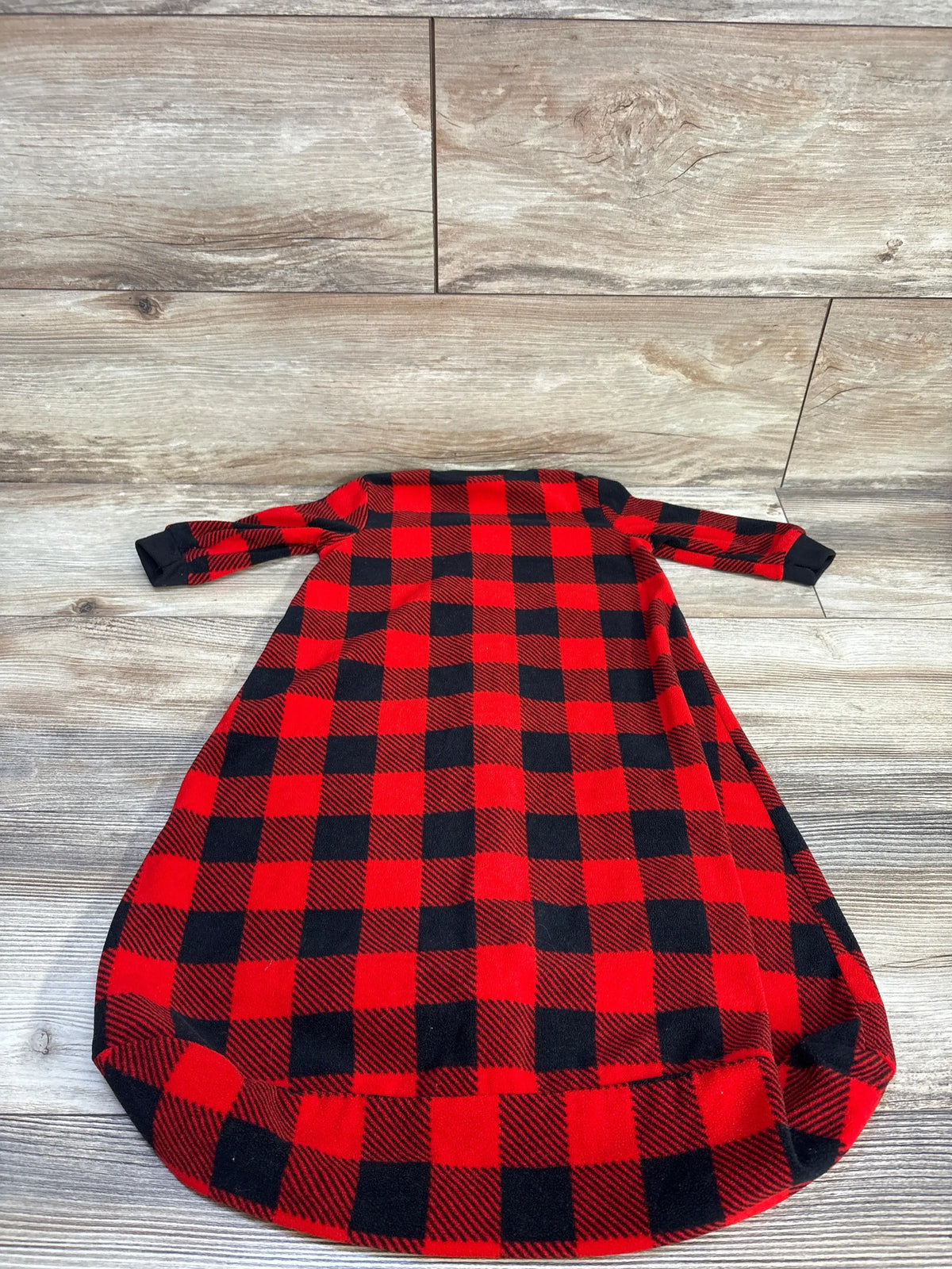 Flat lay of red and black plaid baby sleep sack size 3-6 months showing long sleeves, black cuffs and gathered bottom on wood