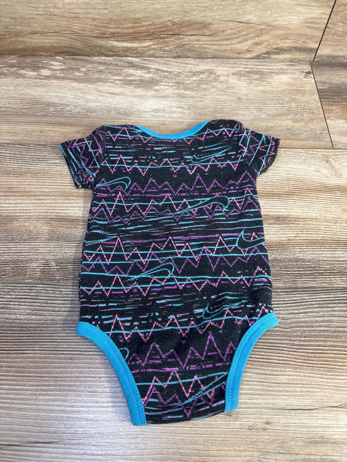 Front view of Nike Bodysuit Black sz 0-6m showcasing colorful zigzag pattern and blue trim on a wood floor