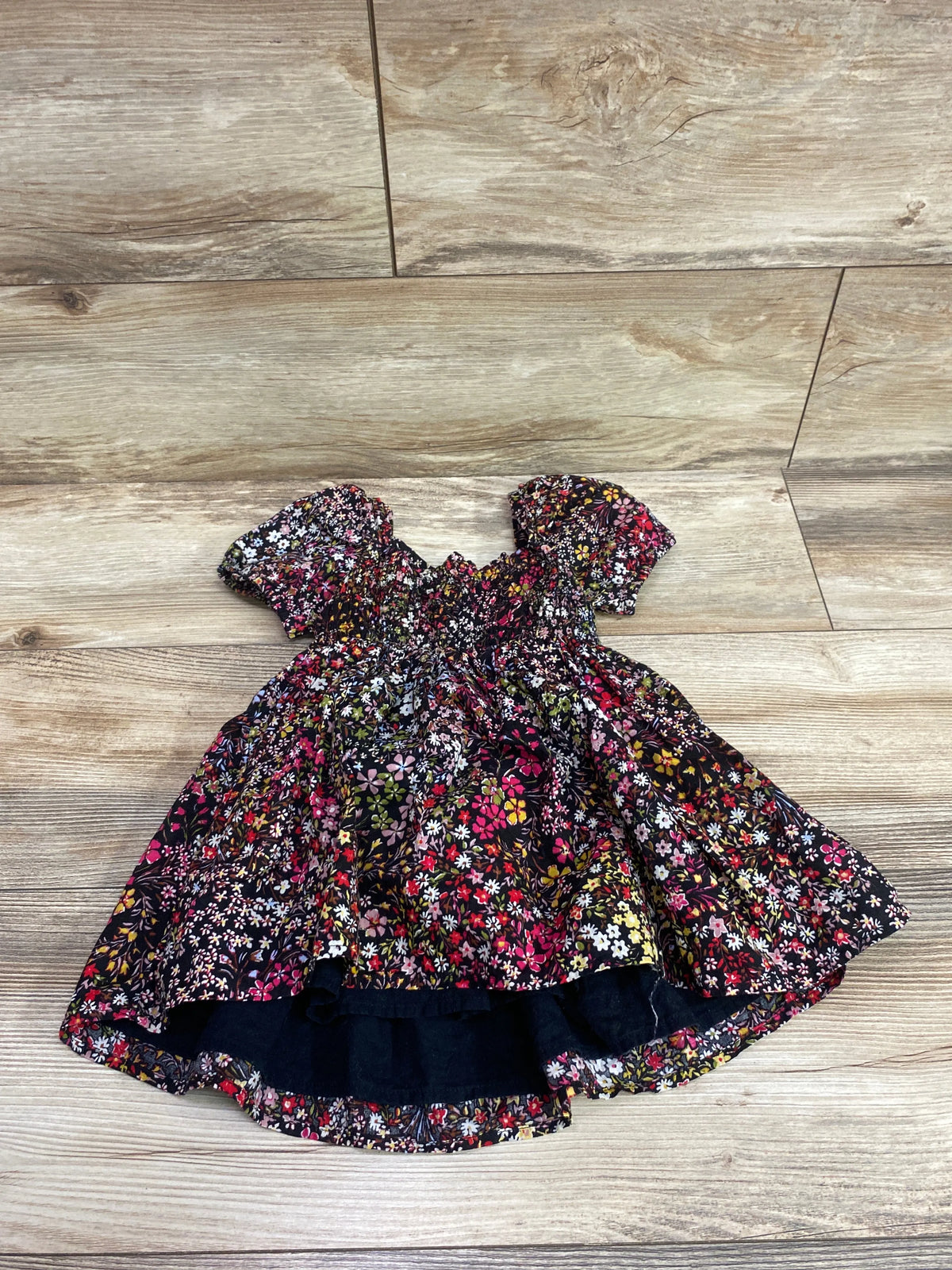 Front view of Baby Gap smocked puff sleeve dress showing floral print on a wood-look floor