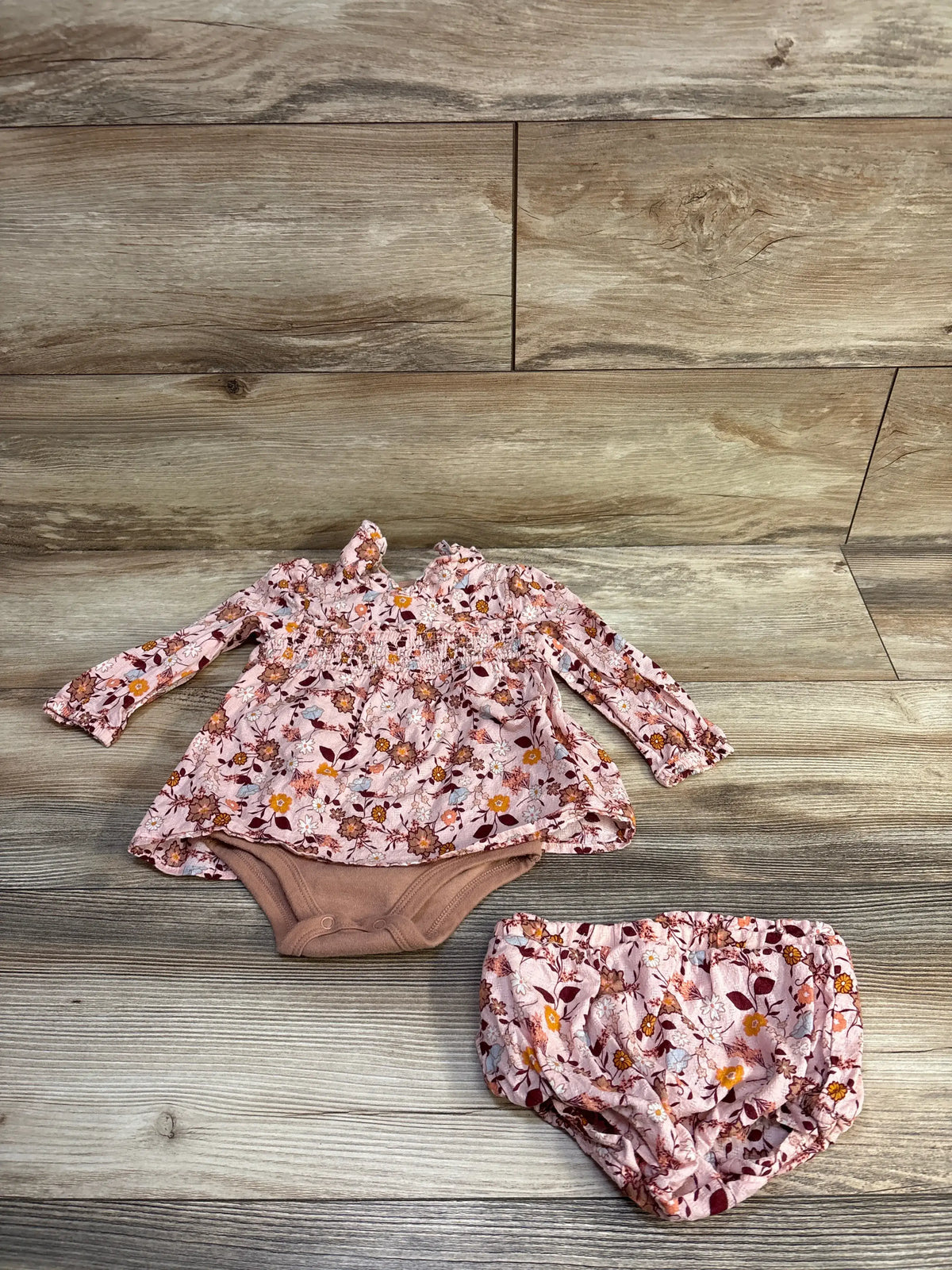 Top view of Nicole Miller pink floral bodysuit dress and bloomers set showcasing long sleeves and a gathered waist on a wood-look floor