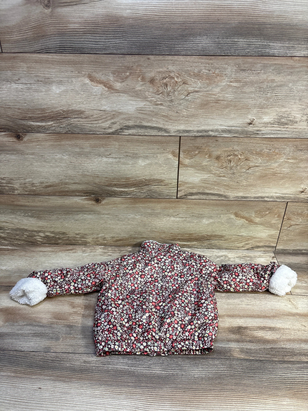 Flat lay of First Impressions floral full-zip lined jacket, 12M, showing brown floral pattern and white fuzzy cuffs on wood