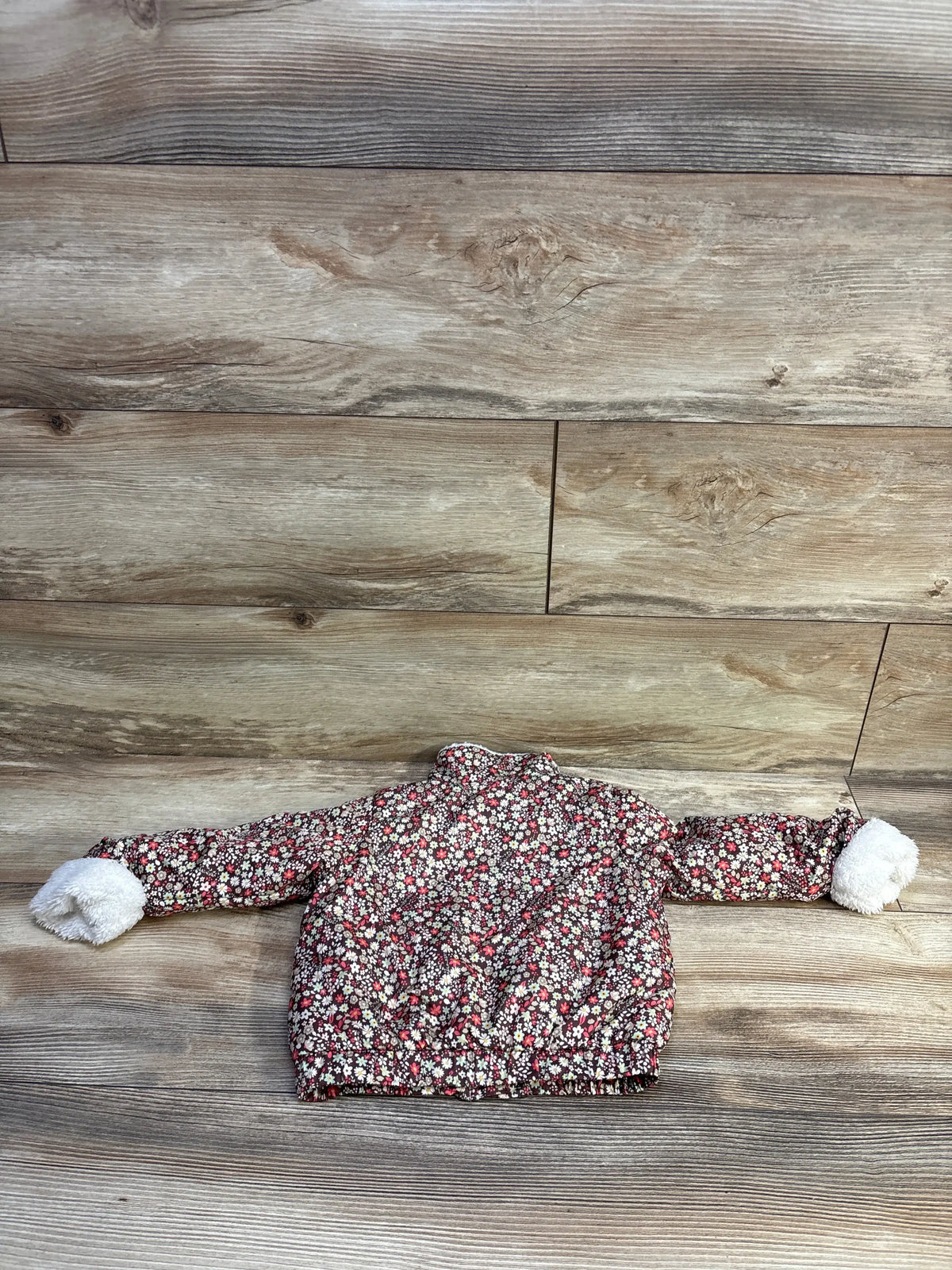 Flat lay of First Impressions floral full-zip lined jacket, 12M, showing brown floral pattern and white fuzzy cuffs on wood