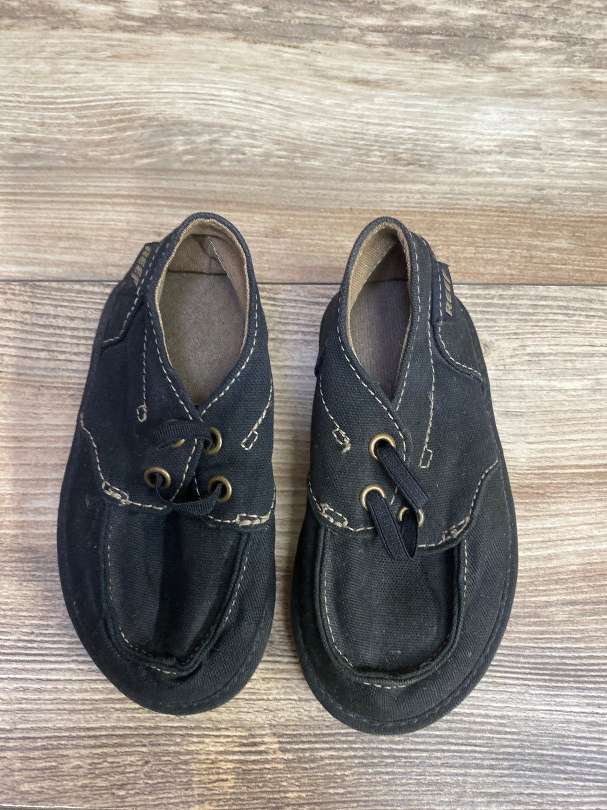 Pair of black toddler canvas shoes with beige stitching on wood surface