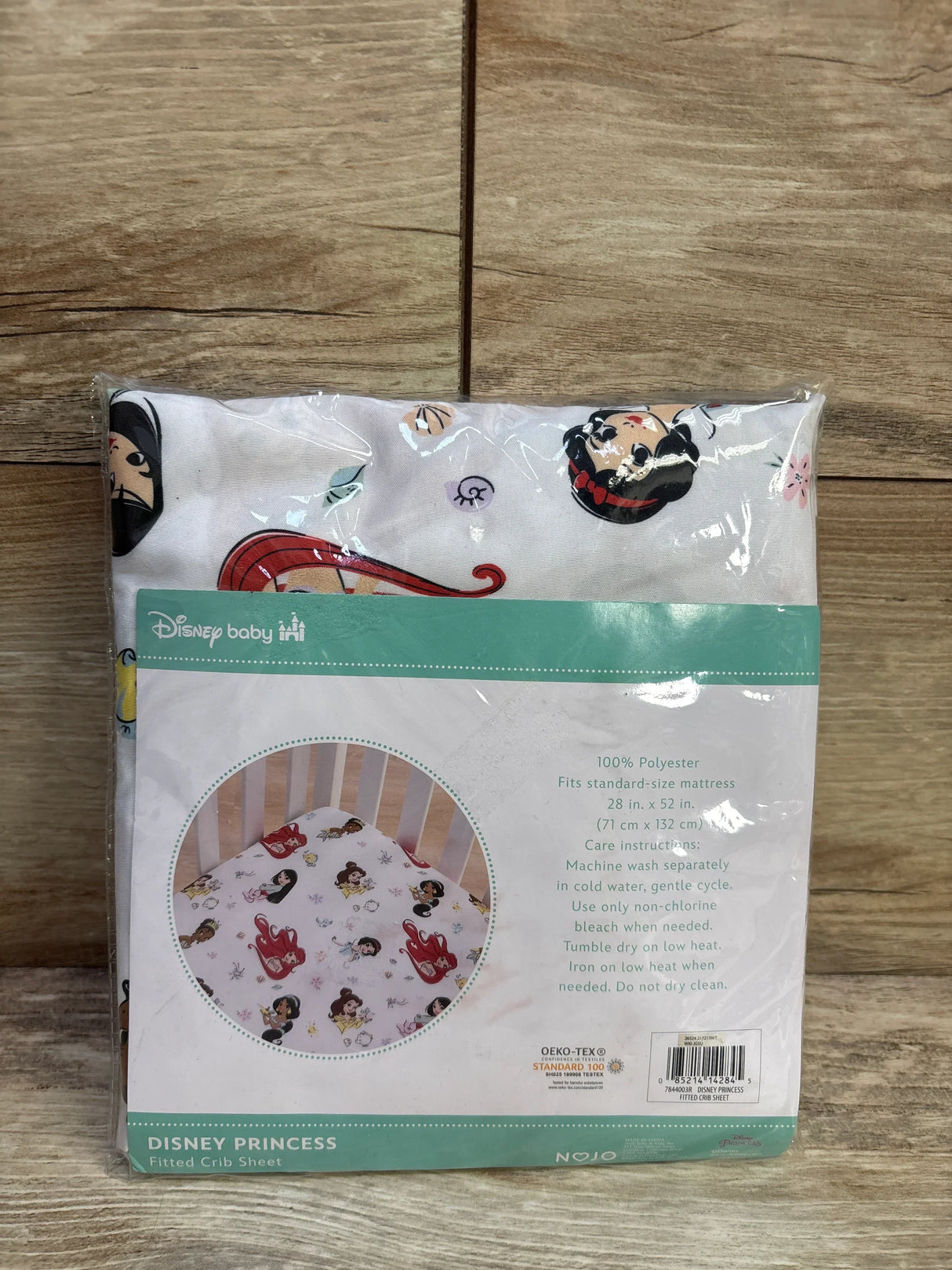 Front view of NEW Disney Baby Disney Princess Fitted Crib Sheet showcasing sealed packaging with princess print on white with pink background