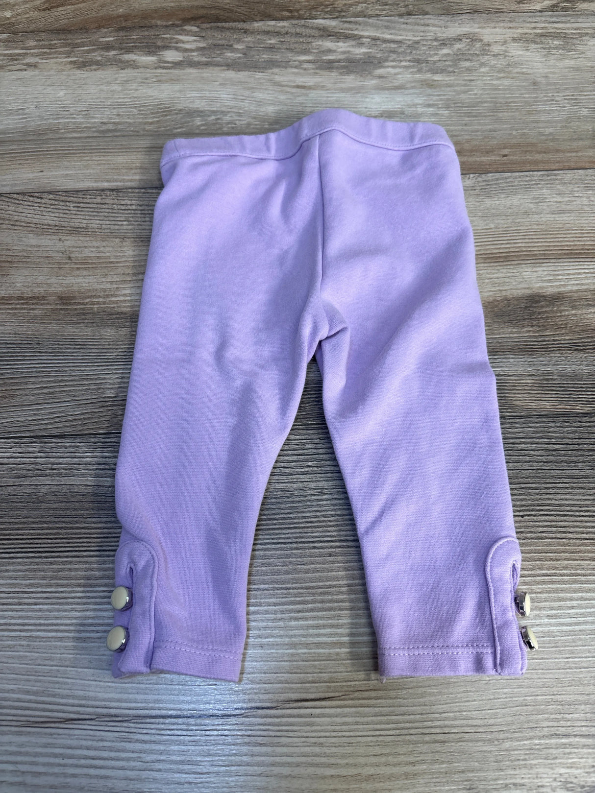 Light purple baby leggings with button details on cuffs, laid flat on wood surface