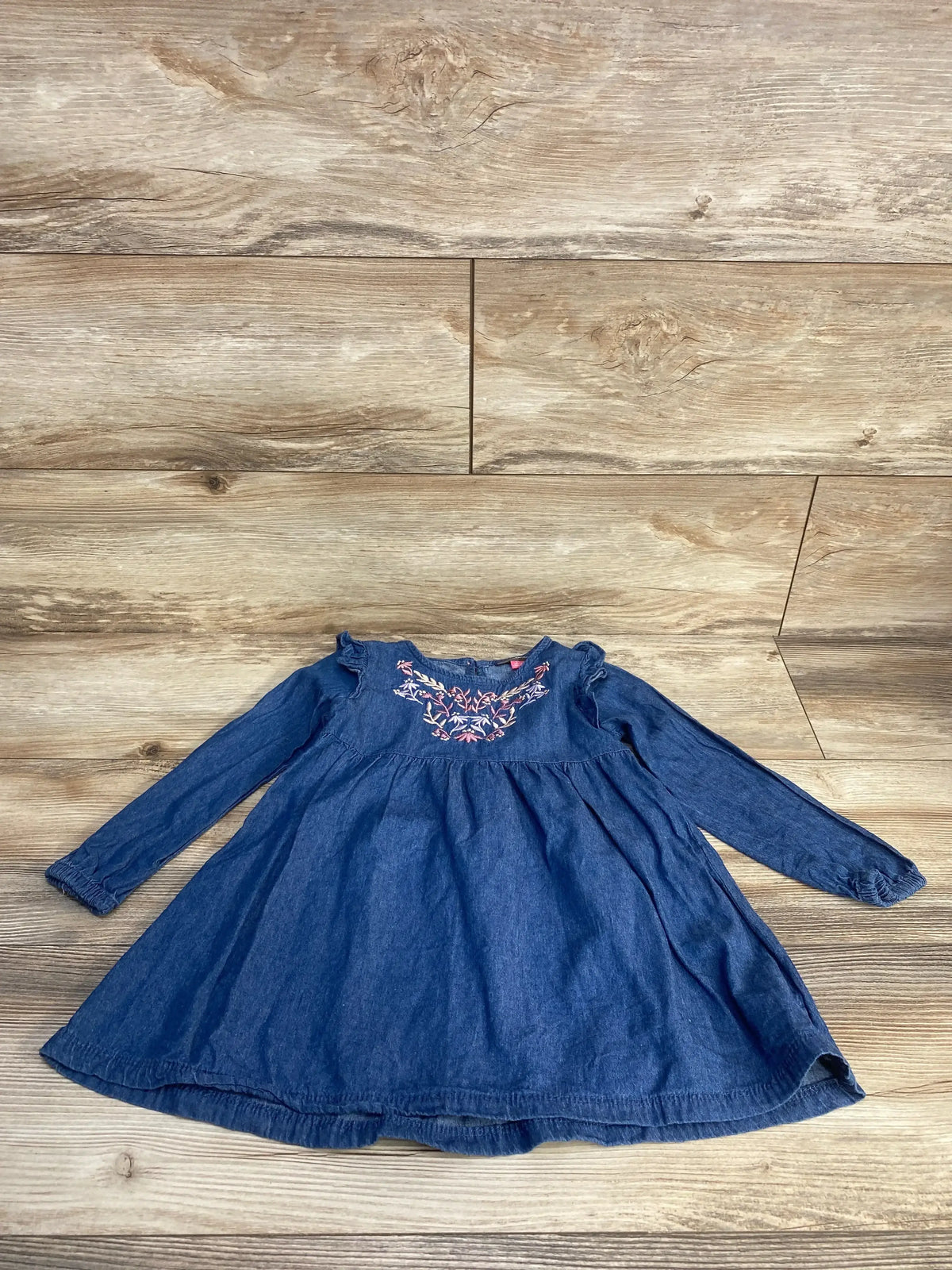 Flat lay of chambray toddler dress size 3T with pink floral embroidery at neckline and long sleeves on wood background