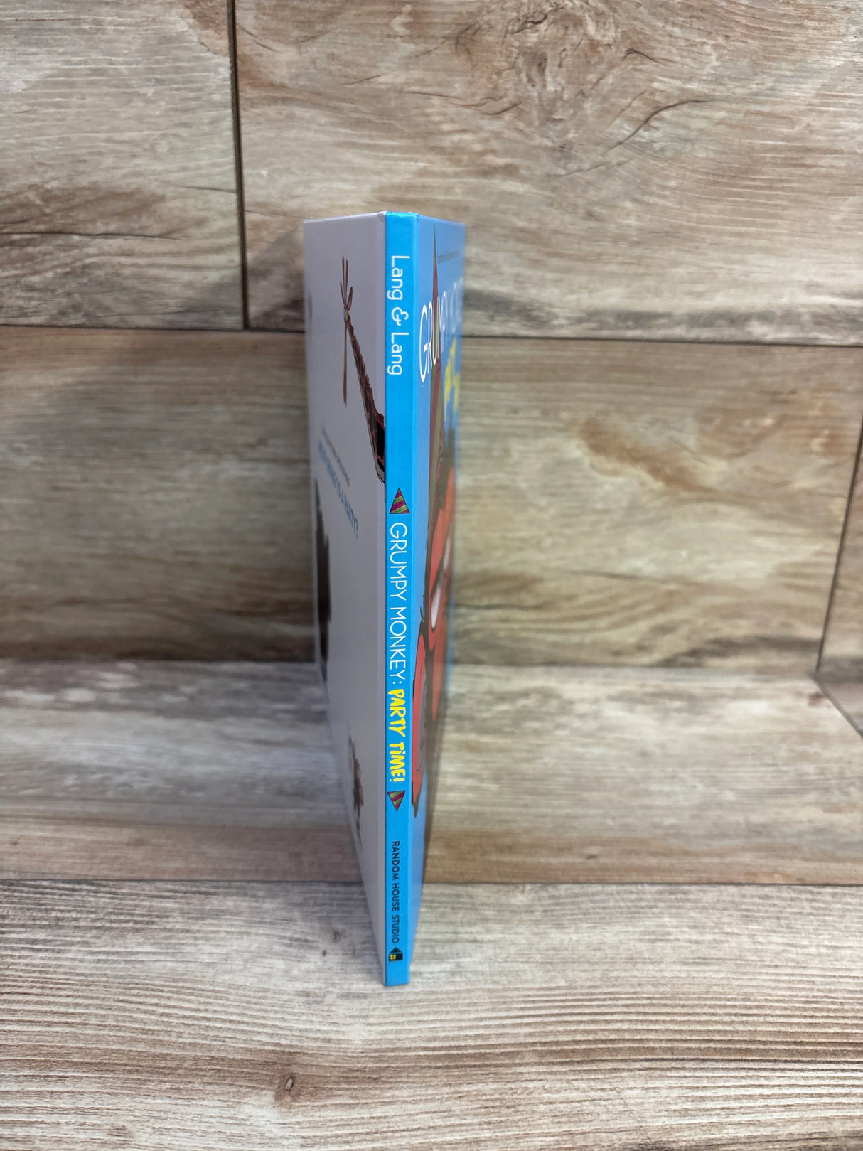 Side view of Grumpy Monkey Party Time! hardcover book showing blue spine and thin board edge on wooden surface