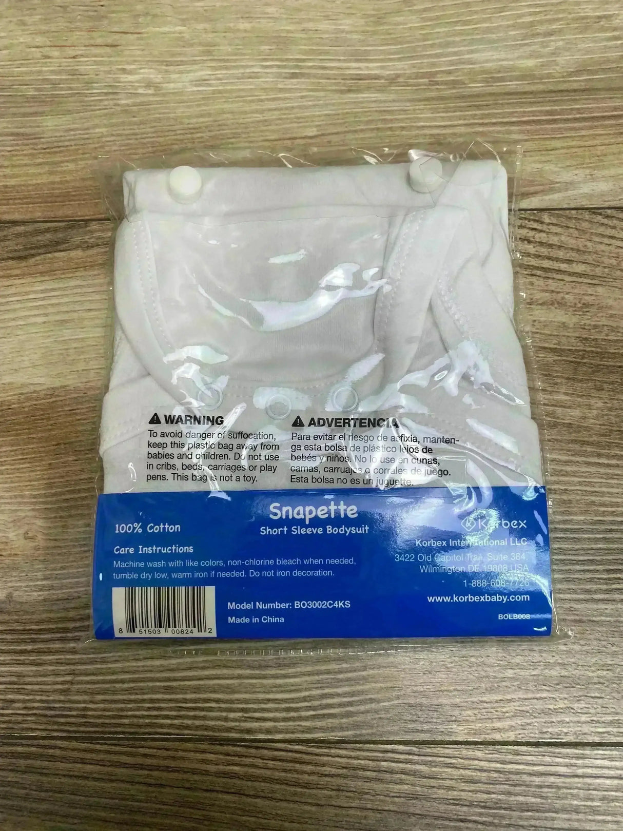 Folded white Snapette cotton short-sleeve bodysuit in clear plastic packaging showing snaps and blue Snapette label