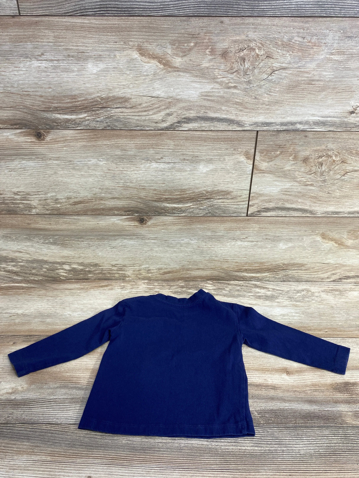 Back view of a navy blue long sleeve toddler shirt on wooden floor background