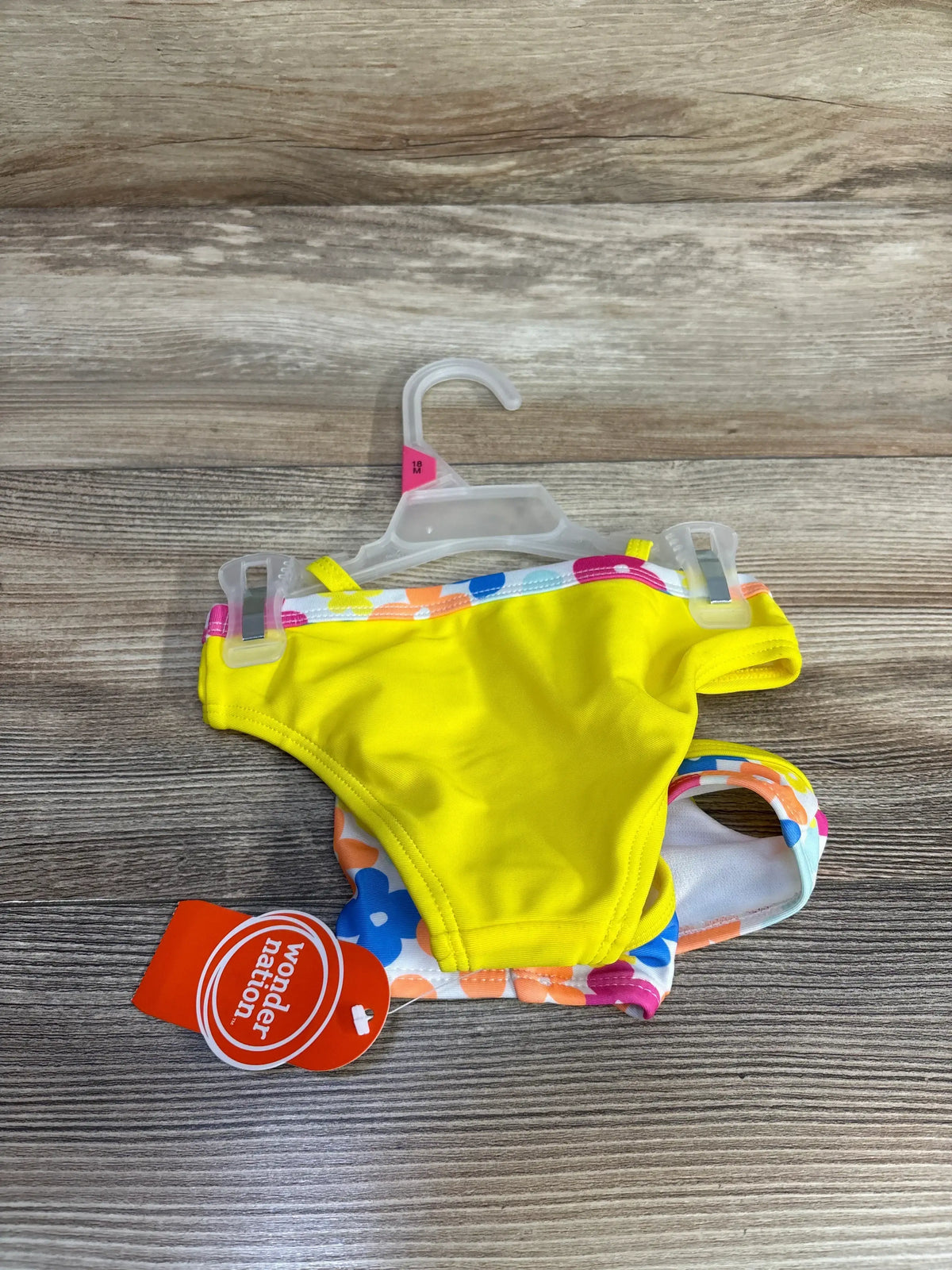 Front view of NEW Wonder Nation 2pc swimsuit in yellow, size 18 months, showing floral bottoms on wood background