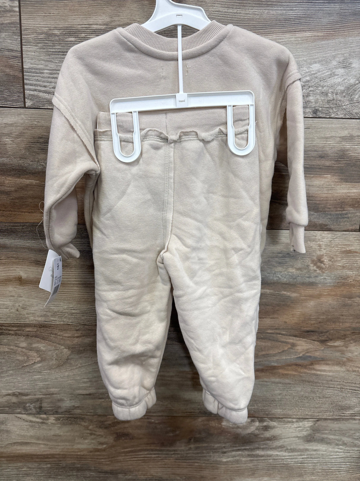 Front view of beige Grayson Mini West Coast fleece crewneck and jogger set in size 2T on a hanger against wood