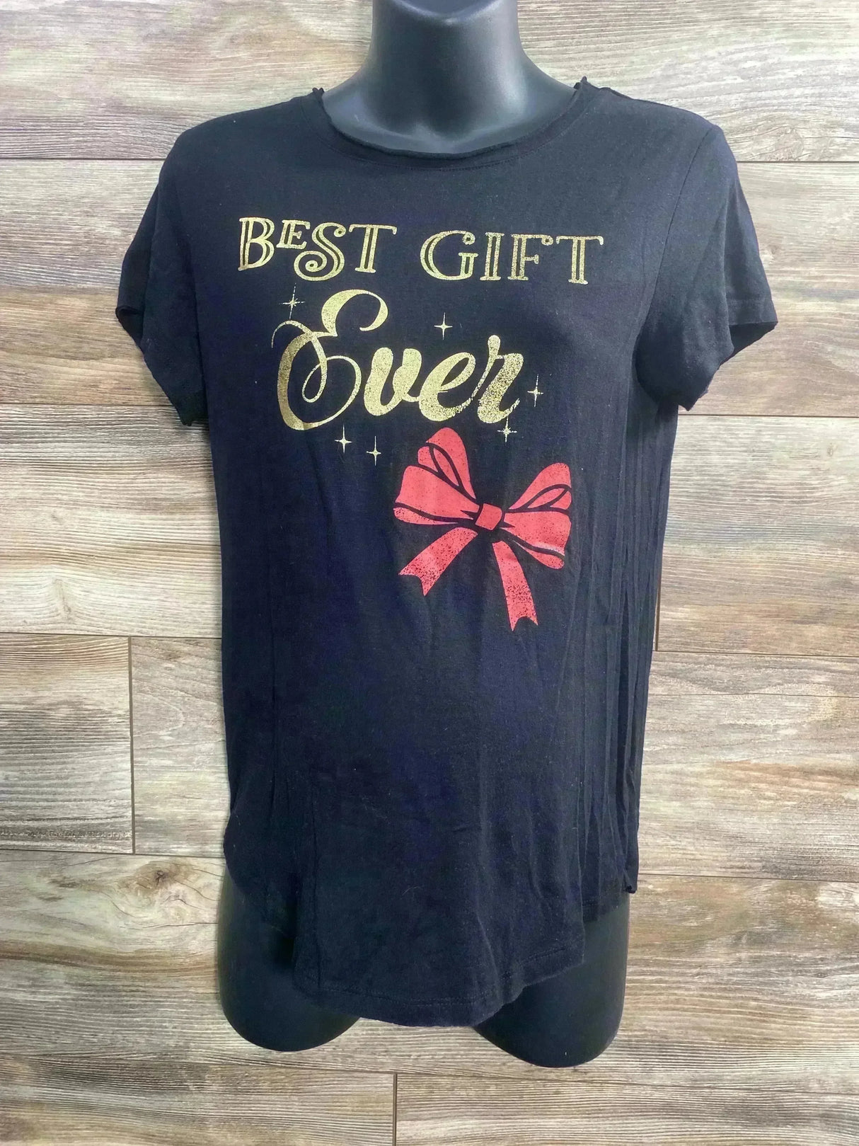 Front view of Isabel maternity black tee showing gold Best Gift Ever lettering and red bow on wood background
