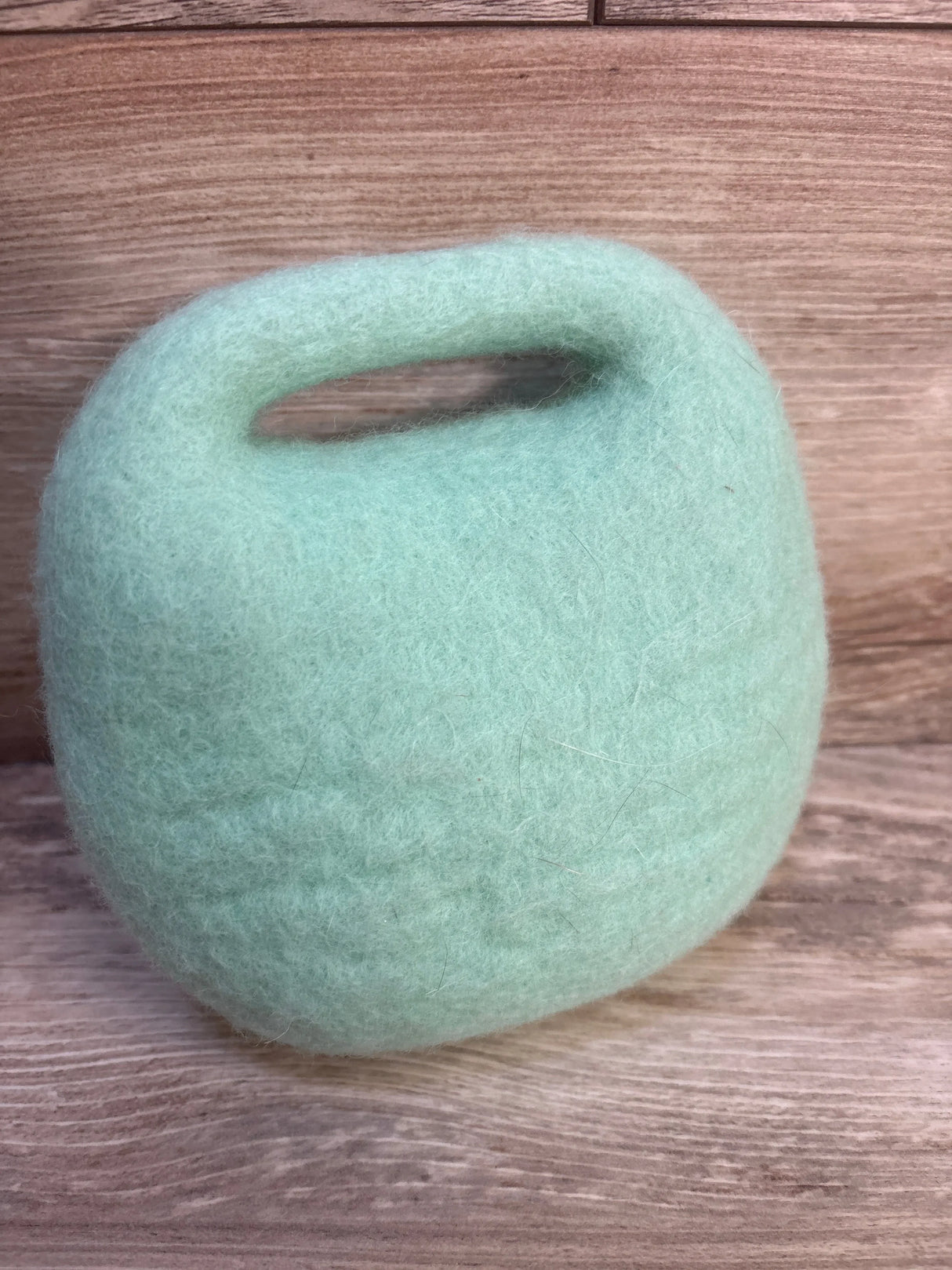 Soft mint green felted wool basket with handle on wood background