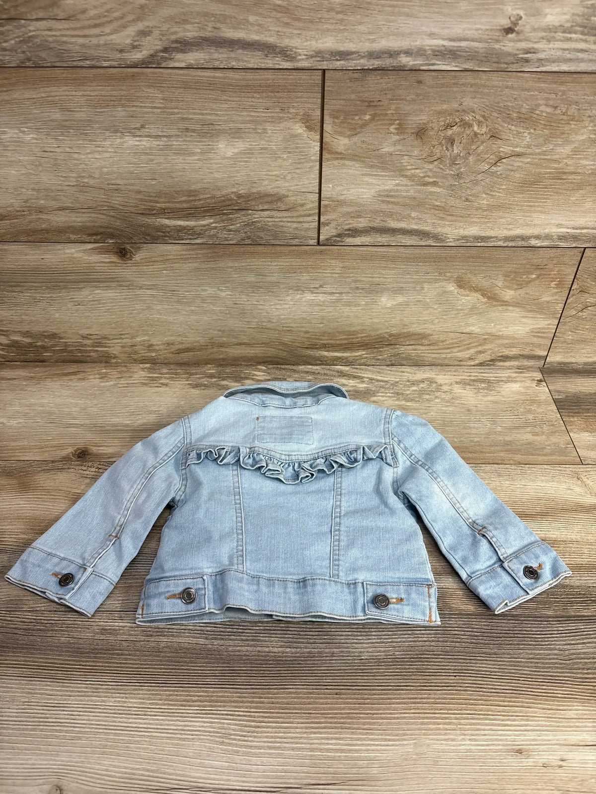 Light blue denim toddler jacket with ruffle detail on back, displayed on wood floor
