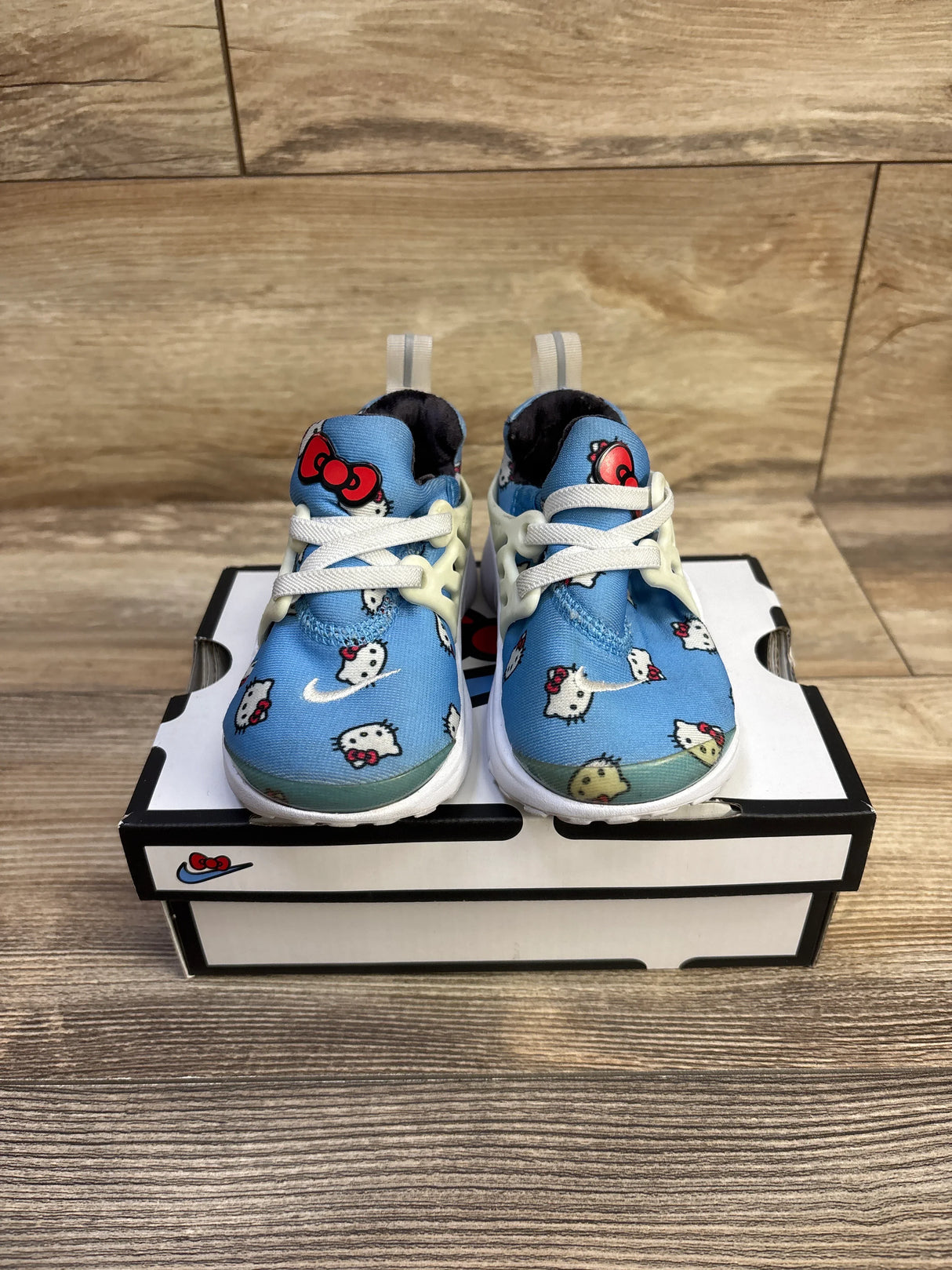 Front view of Hello Kitty x Nike Air Presto toddler sneakers showcasing blue Hello Kitty-print upper and white lace cage with Nike shoebox background