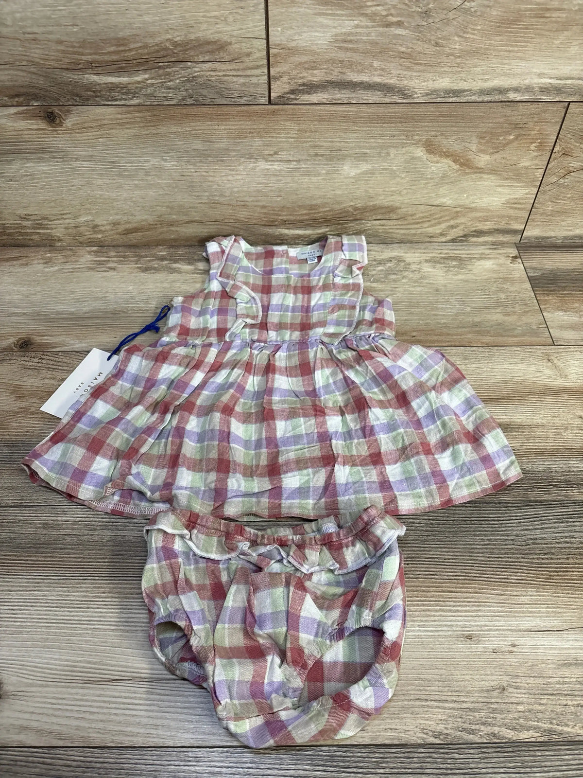 Top-down view of Maison Me Baby pastel plaid ruffle dress and bloomers set showcasing sleeveless design on a wooden floor