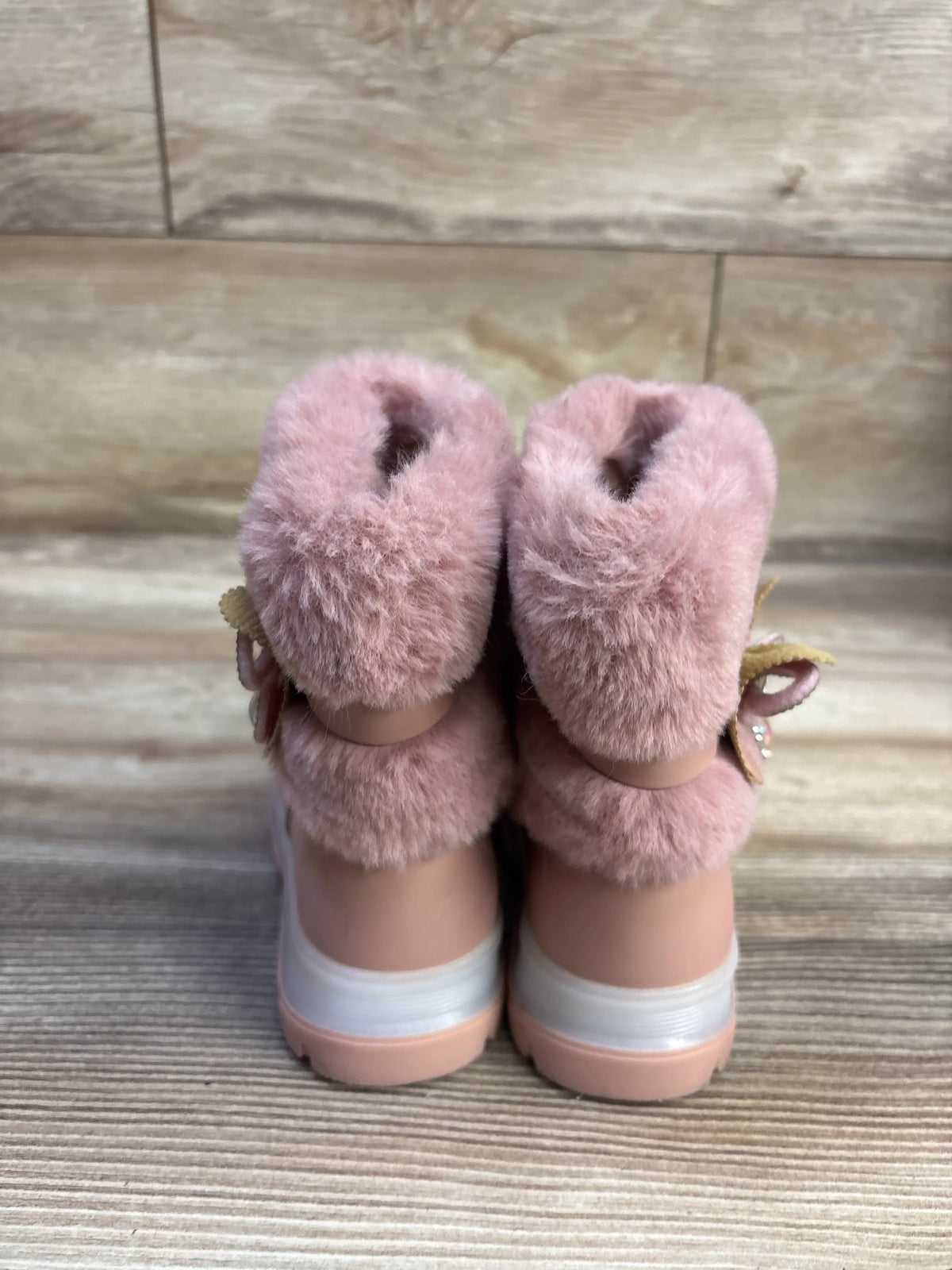 Rear view of Belladia faux fur boots in pink showcasing plush fur cuffs, white heel bands, and pink soles on a wood background