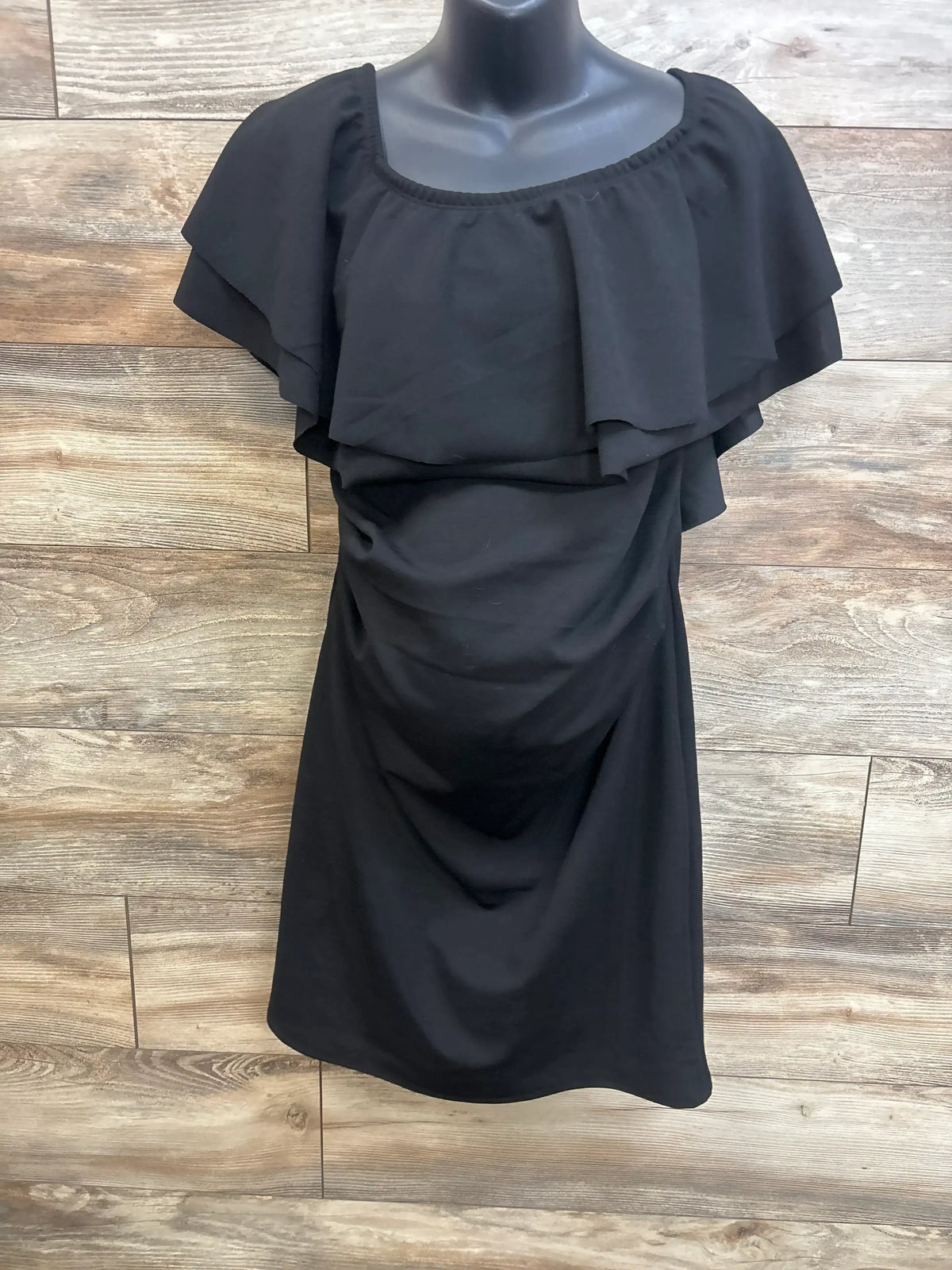 Front view of black My Bump Ruffle Off The Shoulder Dress, size XL, with layered ruffles on wood plank background